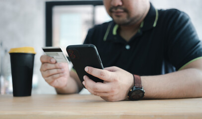 Men use credit cards for shopping payments online on mobile phone applications or websites at cafe. E-commerce and online shopping concept. Online transaction, payment.