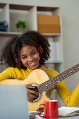 american girl African man wearing headphones while playing guitar in private room and making live video on social media using laptop computer playing happily and relaxing in his own home.