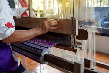 Asian female weavers weaving traditional patterns with hand weaving machines.in the concept of OTOP, community products, hand weaving fabrics, community shops, community weaving centers.