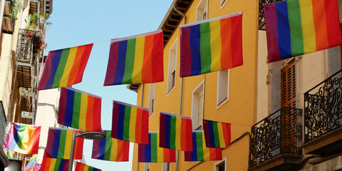 Rainbow flags hang between buildings against clear sky. Symbol of tolerance and acceptance of LGBTQ community. During gay pride in Madrid, Spain