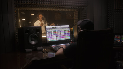 African American man in professional headphones sings new song to microphone in sound recording...