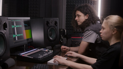 Female audio engineer and musician create song in music recording room. Computer screen showing DAW...