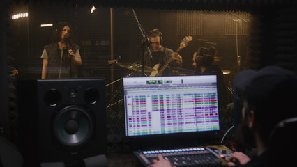 Musical band records song in recording room. Sound engineer or producer uses control surface....