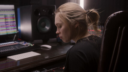 Female sound engineer, musician uses MIDI controller, digital electric piano for creating music. Computer screen shows DAW software interface with sound tracks. Recording studio. Music production.