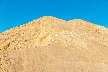 A high mountain of sand in a quarry against a blue sky. Stock of bulk building materials. A big pile of sand and gravel. Photo in high resolution. A quarry for sand extraction in the photo. Sand hill.