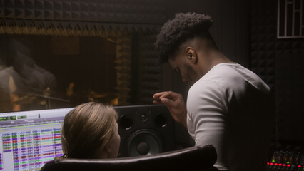 Experienced audio engineer and African American producer work with singer in sound recording...