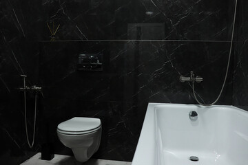 A white bathtub in a dark gray marble bathroom. Modern luxury bathroom.