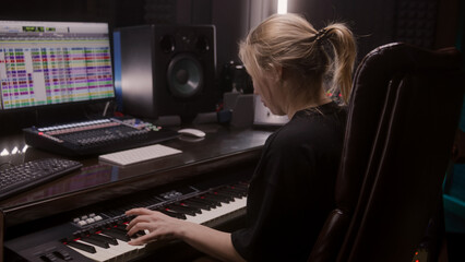 Female sound engineer, musician uses MIDI controller, digital electric piano for creating music. Computer screen shows DAW software interface with sound tracks. Recording studio. Music production.