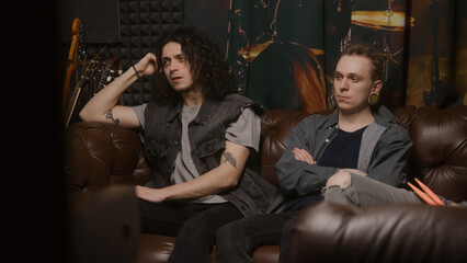 Fototapeta na wymiar Musical rock band sits on couch. Stylish male musicians, artists, performers listen to ready recorded songs for new album in professional sound and music recording studio. Concept of music production.