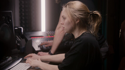 Female sound engineer uses mixing console, creates new song or DJ set with producer in sound...