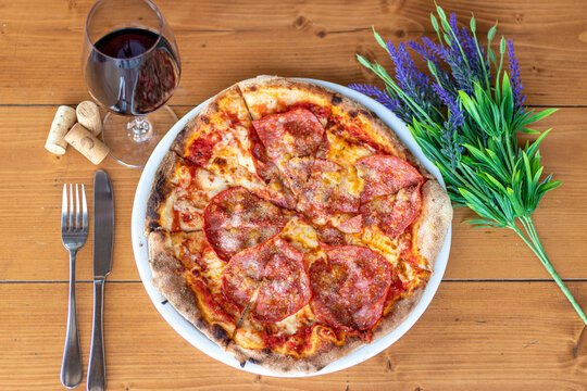 Frische hausgemachte italienische Pizza Salami mit einem Glas Wein an einem dekorierten Tisch