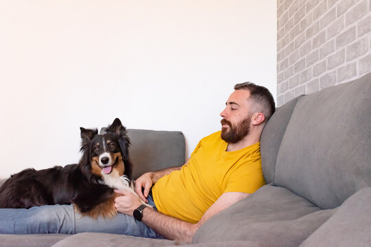 Young man lying on the sofa at home with his dog lying at his feet.