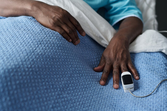Close-up of patient checking oxygen in blood with pulse oximeter on his hand while lying on bed in ward - Powered by Adobe