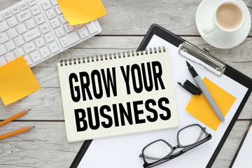 Grow your business text on white paper near the keyboard and feminine stickers. light wooden background