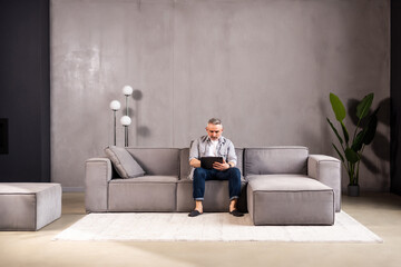 Attractive man relaxing on a sofa with a tablet-pc reading or watching media with a quiet smile