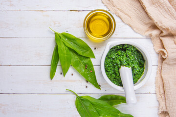Fresh bear garlic also known as wild garlic or ursinum allium pesto crushed in a mortar and oil on a wooden table with white boards and beige kitchen table cloth