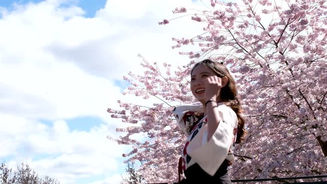beautiful asian woman laughing throwing her hair in wind against backdrop of cherry blossoms and blue sky with white clouds embroidered japanese national dress chinese korean bright face young girl
