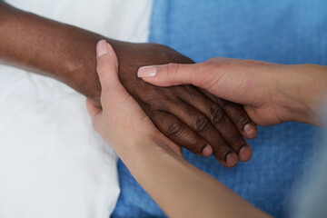 Close-up of young nurse holding hands with elderly African American man and supporting him during his disease