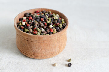 Fototapeta na wymiar A mix of black, white, red and allspice peppercorns in a wooden bowl on a light background. dried spice peppercorn concept. Horizontal orientation. Copy space.