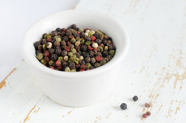 A mix of black, white, red and fragrant peppercorns in a white bowl on a light background. dried spice peppercorn concept. Horizontal orientation. Selective focus.