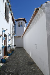 Una calle blanca en Granada con macetas y torre de mezquita al fondo