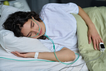 Young woman sleeping with oxygen tube on bed in hospital ward