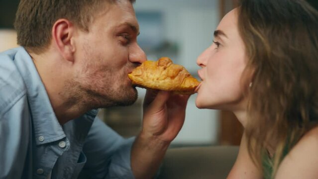 Romantic pair eating croissant home zoom on. Loving man woman face bitting bun
