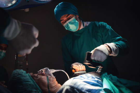 Doctors and team performing using defibrillator to give electrical shock wave to patient heart in bright Modern operating room with lighting equipment at hospital.