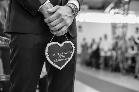 Uno sposo tiene in mano un cuore con la scritta in Italiano  "la tua sposa sta arrivando"