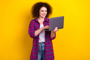 Photo of cheerful cute lady wear plaid magenta trendy jacket hold her new laptop multitask device for job isolated on yellow color background