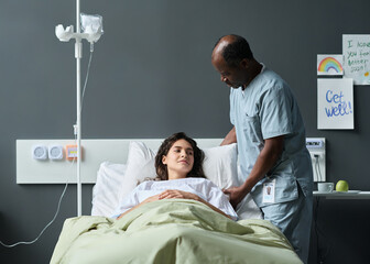 Male nurse caring about sick patient while she lying on bed in hospital ward