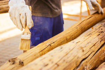 A faceless master carpenter works with wood by treating a surface with glue to protect it from...