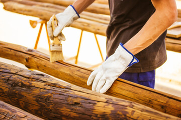 A faceless master carpenter works with wood by treating a surface with glue to protect it from...