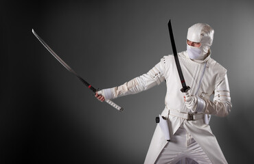 Ninja poses for a photo on a gray background, a male ninja in a white kimono © AleksFil