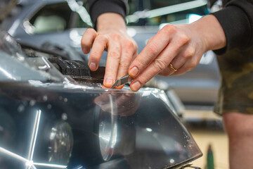 The process of installing a protective polyurethane film for paint on the front headlight of a car. PPF is a polyurethane film that helps protect glass and metal from scratches. Selective focus.  