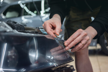 The process of installing a protective polyurethane film for paint on the front headlight of a car. PPF is a polyurethane film that helps protect glass and metal from scratches. Selective focus.  