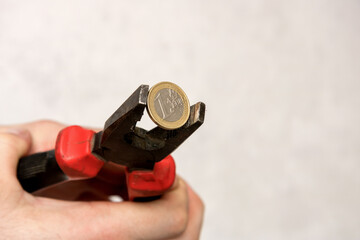 man's hand holds 1 euro in a vice, financial crisis