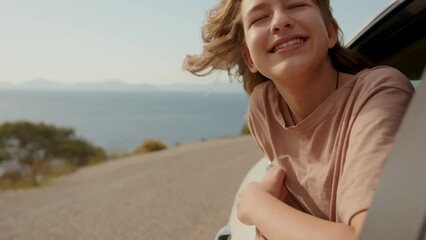 Child leaned out of car window smiling with pleasure. School age girl smiling carelessly and enjoying journey. Happy family travel concept