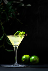 Gimlet alcoholic cocktail with dry gin, liqueur, lime juice and ice in glass garnished with lime zest. Black background