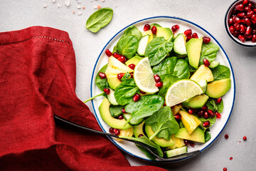 Vegan salad with pineapple, spinach, avocado and pomegranate, gray table, top view. Healthy eating, clean food, diet, weight loss concept