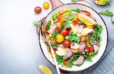 Canned tuna salad with cherry tomatoes, red onion, eggs, sweet corn, paprika, lettuce, radicchio and arugula. Gray table background, top view