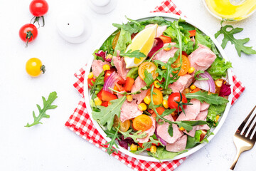 Canned Tuna salad with colorful cherry tomatoes, red onion, sweet corn, paprika, lettuce, radicchio and arugula. White table background, top view