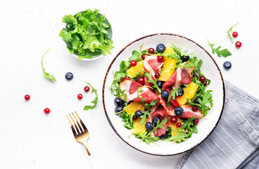 Gourmet salad with smoked duck fillet, fruit and berries, arugula and lettuce, white table background, top view