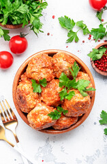 Pork and beef meatballs in tomato sauce in wooden bowl on white table background, spices and herbs. Delicious home cooking. Top view