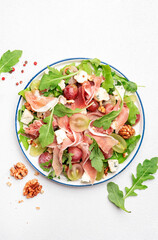 Fresh grape salad with jamon, blue cheese, arugula, nuts on white table background, top view, copy...