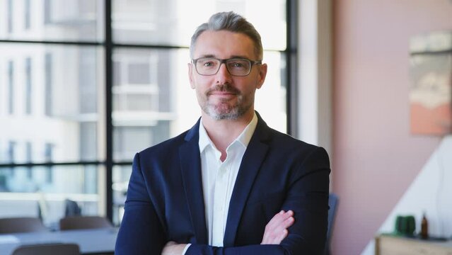 Portrait of serious mature businessman wearing glasses standing in empty modern open plan office looking into camera - shot in slow motion