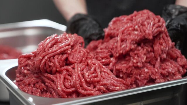 The seller puts the fresh ground beef into an iron container. minced meat in the hands of the chef.