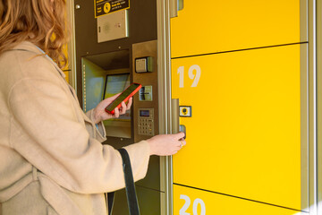 Close-up of blonde traveller woman with smart phone opens or closes a numbered storage box in a public place. New business locker self service storage Mass Transit system for help people and travelers