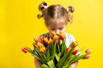 a small blonde girl on a yellow background with a bouquet of red tulips in her hands, smiling. holiday concept