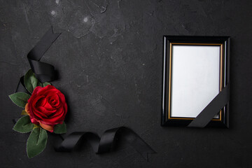 top view of black bow with red flower and picture frame on a dark surface funeral death